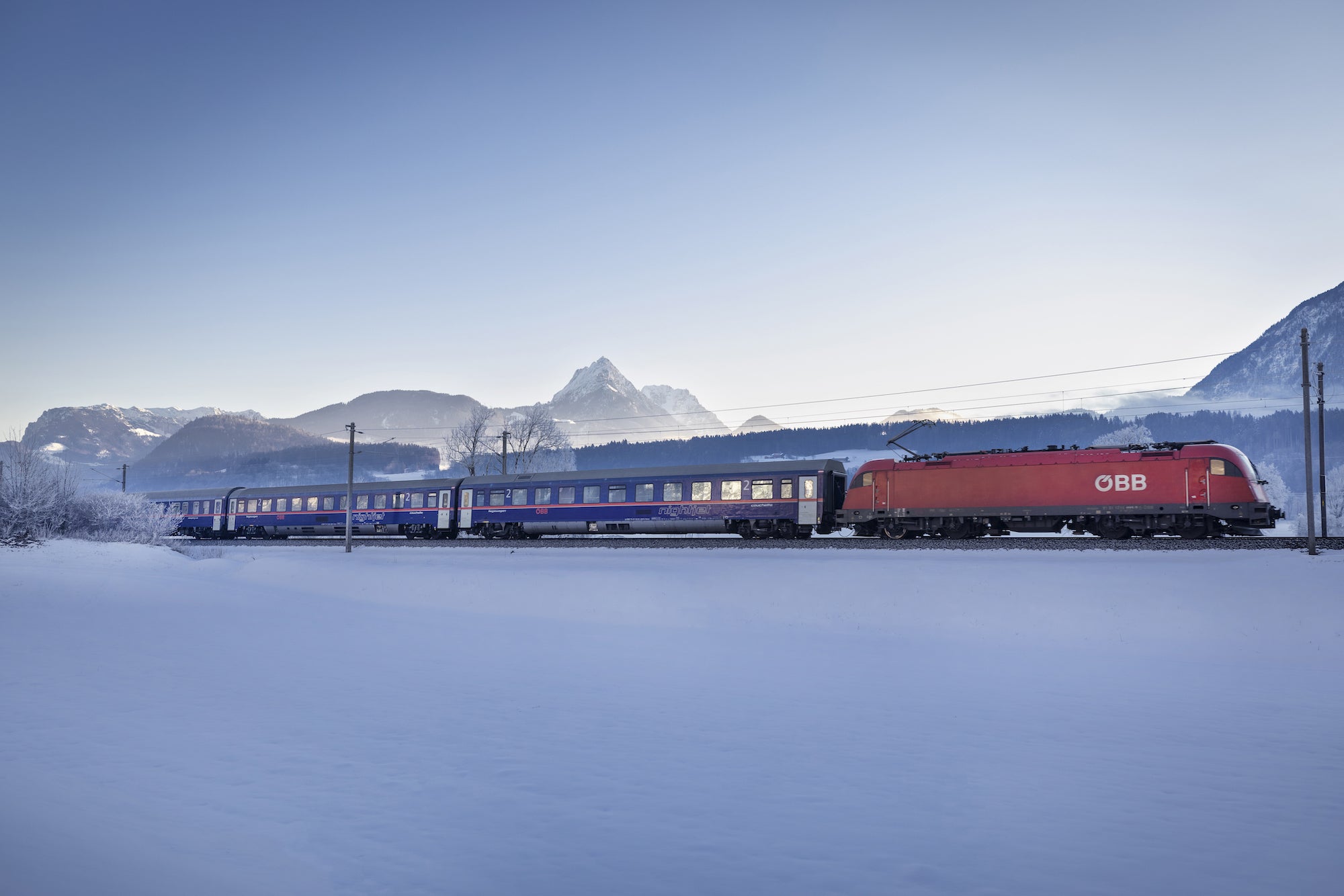A red Austrian OBB train travelling through the snow.